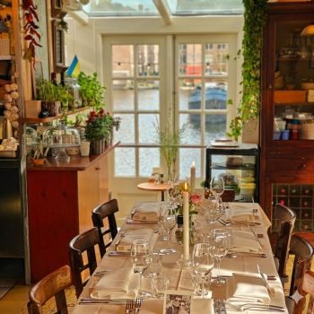 Long table set for an intimate group dinner at Markerhuisje Amsterdam, featuring a cozy, homey atmosphere and direct waterfront view of the canals.